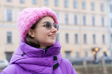 A woman wearing a pink hat and a purple coat is smiling. She is wearing sunglasses and has a pink scarf around her neckの写真素材