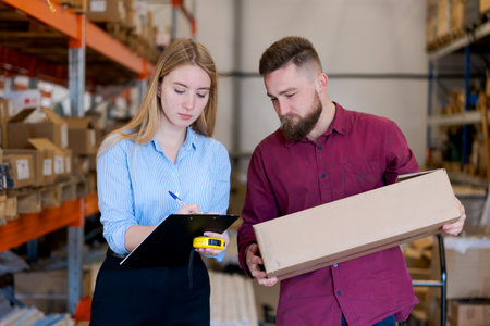 Professional logistics managers checking stock. Female supervisor writing on a clipboard while male...