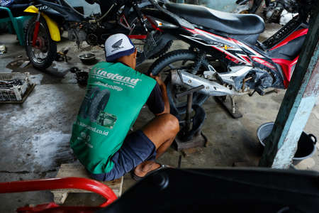 Lampung, Indonesia, March 13, 2022: An Asian man works as a repair shop mechanic repairing motorbikesのeditorial素材