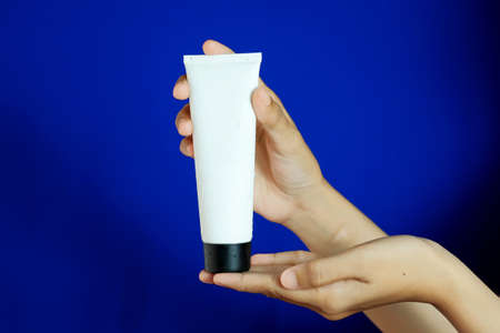 Woman holding the bottle or tube with spa cosmetics on blue background. Beauty blogger, salon...