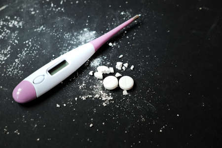 White pill and thermometer on dark background. Copy space
