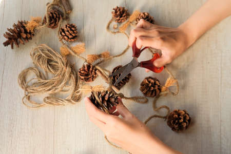Part of a woman's hands making wall hangings from pine cones and jute rope