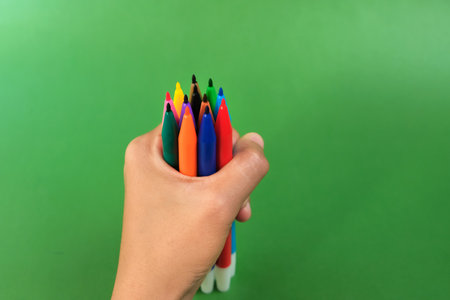 Human hand holding bunch of colorful markers on green background. Concept of creativity, drawing, bright worldの写真素材