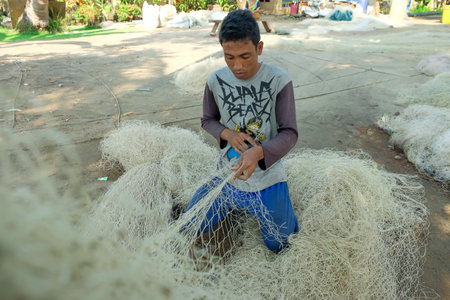 Lampung, Indonesia, October 16, 2022: Commercial fishermen repair or embroider damaged nets in a drying area. Lifestyle concept of indigenous ethnic groups in Indonesiaのeditorial素材