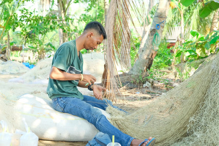 Lampung, Indonesia, October 16, 2022: Commercial fishermen repair or embroider damaged nets in a drying area. Lifestyle concept of indigenous ethnic groups in Indonesiaのeditorial素材