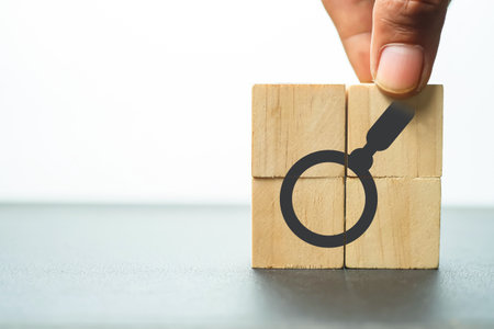 Hand holding magnifying glass and wood cube block with magnifying glass symbol. Searching concept.の写真素材