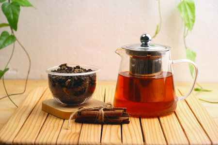 tea in a glass teapot and cinnamon on a wooden tableの写真素材
