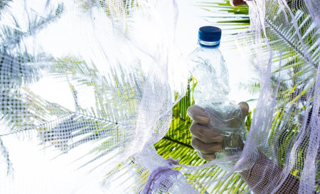Man hand holding a plastic bottle of water on a palm tree backgroundの写真素材