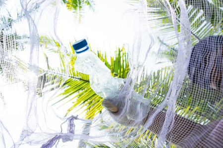 Man holding plastic bottle in the hammock with palm tree background.の写真素材