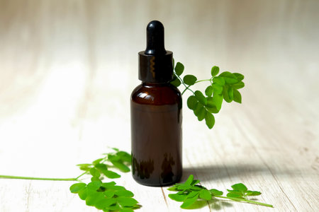 Moringa essential oil in a brown glass bottle with fresh leaves.の写真素材