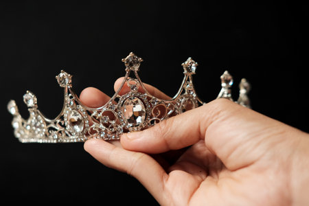 Male hand holding a silver crown on black background, close-upの写真素材