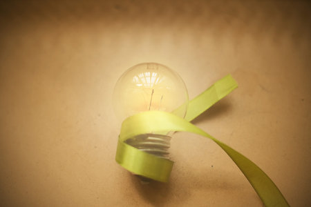 Incandescent light bulb with green ribbon on a brown paper backgroundの写真素材