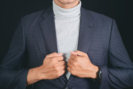 Businessman in suit buttoning his sleeve on black background, closeupの写真素材