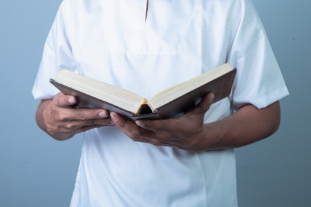 Man reading a holy book Koran on blue background. Close-up of male hands.