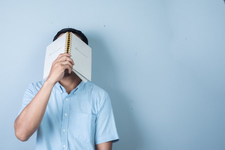 Asian man wearing blue shirt reading a book on blue background. Education concept.の写真素材