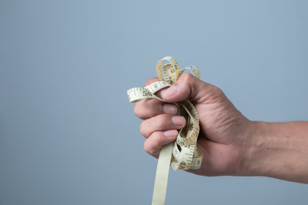 Man's hand holding a measuring tape on a gray background, close upの写真素材