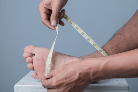 Close up of man measuring his feet with tape measure on grey backgroundの写真素材