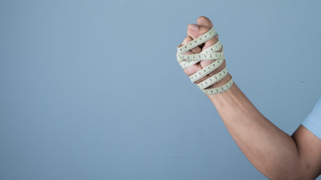 Man hand with measuring tape on blue background, weight loss concept.の写真素材