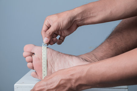 Close up of man measuring his foot with a measuring tape on grey backgroundの写真素材