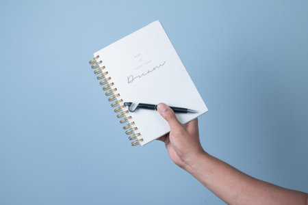 Hand holding a pen and notebook on blue background, business conceptの写真素材