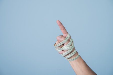 Man's hand in bandage with measuring tape on blue background. Dieting concept.の写真素材