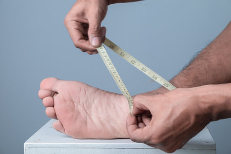 Close up of man measuring his foot with a tape measure on grey backgroundの写真素材
