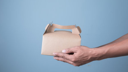 Man hand holding cardboard box on blue background, food delivery concept.の写真素材