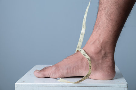Man measuring his bare feet with a tape measure on a grey backgroundの写真素材