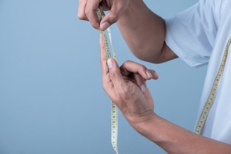 Man measuring waist with tape measure on blue background. Diet and weight loss concept.の写真素材