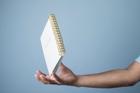 Hand holding a notebook isolated on a blue background with clipping path.の写真素材