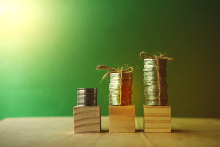 Stack of coins and wooden blocks on green background, business growth concept.の写真素材