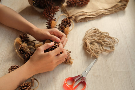 Female hands making christmas wreath with pine cones and twine