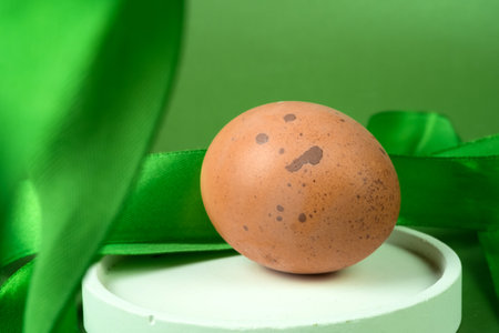 Easter egg with green satin ribbon on a green background.