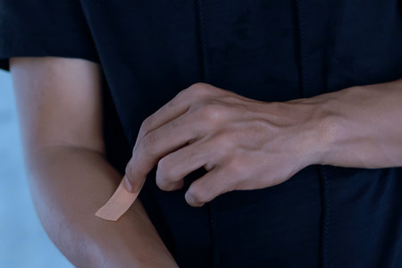 A man putting a plaster on his arm against an abstract light blue background