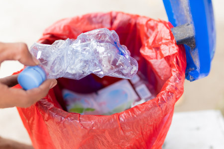 Male hand throwing empty plastic water bottle into recycling binの写真素材