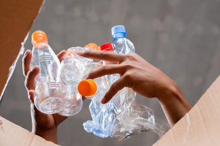 A man collects and puts recyclable plastic bottles in a cardboard box