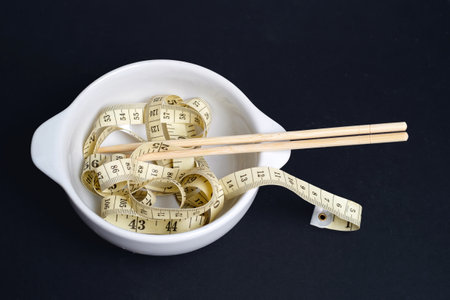 Measuring tape and chopsticks in a white bowl. Weight control concept