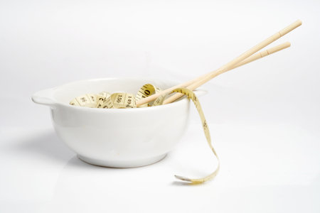 Measuring tape and chopsticks in a white bowl. Weight control conceptの写真素材
