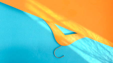 Empty wooden clothes hanger on pastel orange and blue background in sunlight, copy space. Sale and shopping concept.の写真素材