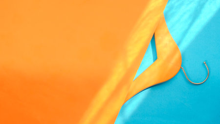 Empty wooden clothes hanger on pastel orange and blue background in sunlight, copy space. Sale and shopping concept.の写真素材