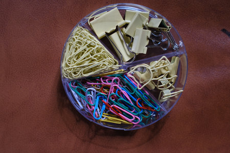 Paper clips and paperclips in a plastic box on a brown background