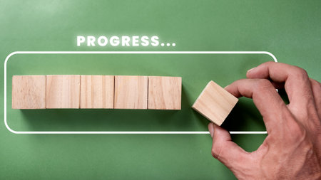 Hand laying wooden cube blocks on light green background and with loading graphics. Job progressive conceptの写真素材