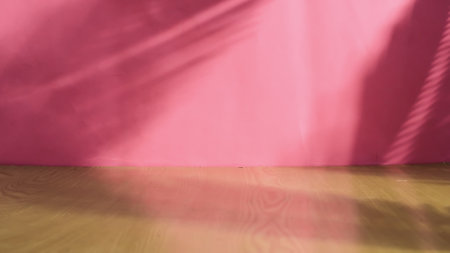 Empty wooden floor and pink wall with shadow from a palm leaf.