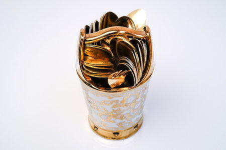 golden spoon and fork in a metal cup on a white backgroundの写真素材