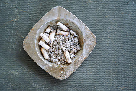 Overhead View Of A Metal Ashtray Filled With Cigarette Butts On A Dark Grey Surfaceの写真素材