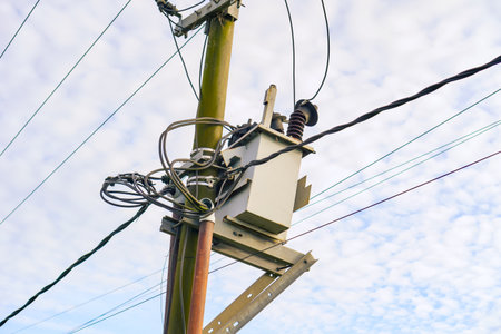 Gray Electrical Transformer Mounted On Rustic Utility Pole Against Cloudy Skyの写真素材