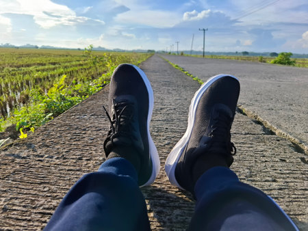 Person Relaxing in Shoes on a Country Road Overlooking Rice Fieldsの写真素材