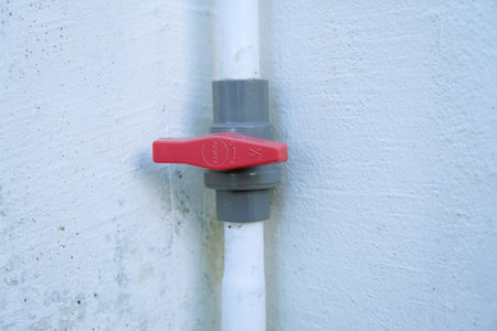 Plastic water tap with red handle on the white wall background.の写真素材