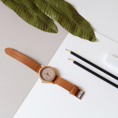 Top view of wooden watch on pastel color background. Artificial leafs, back pencils land leather band watch on soft color background.の写真素材