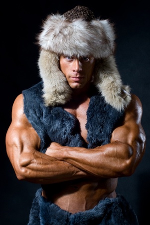 Strong athletic man in a fur cap isolated over black backgroundの写真素材